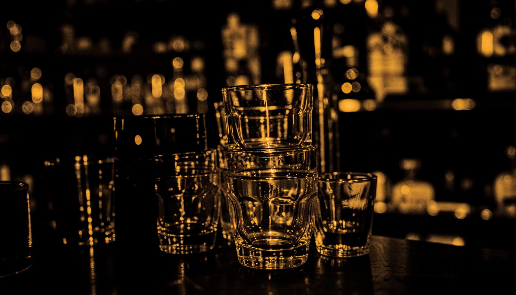 Soft amber and black duotone of stacked empty pint glasses catching warm light, dark bar background