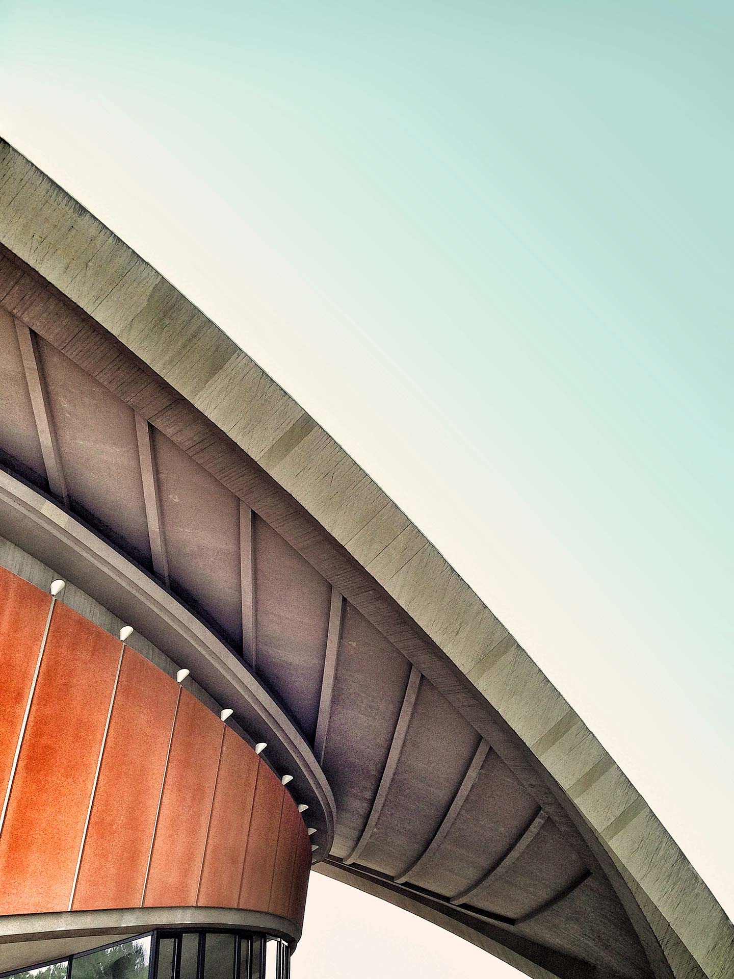 Duotone photograph of a curved architectural overhang with rust-orange panels against a pale teal sky, modern and architectural.