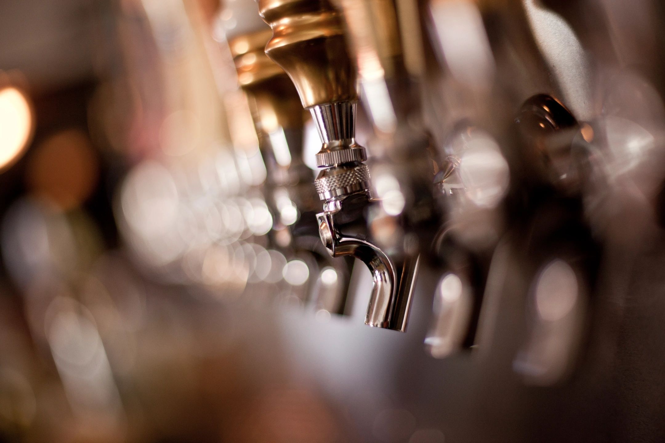 Hard amber and black duotone of a row of beer taps with warm bokeh, dark bar atmosphere